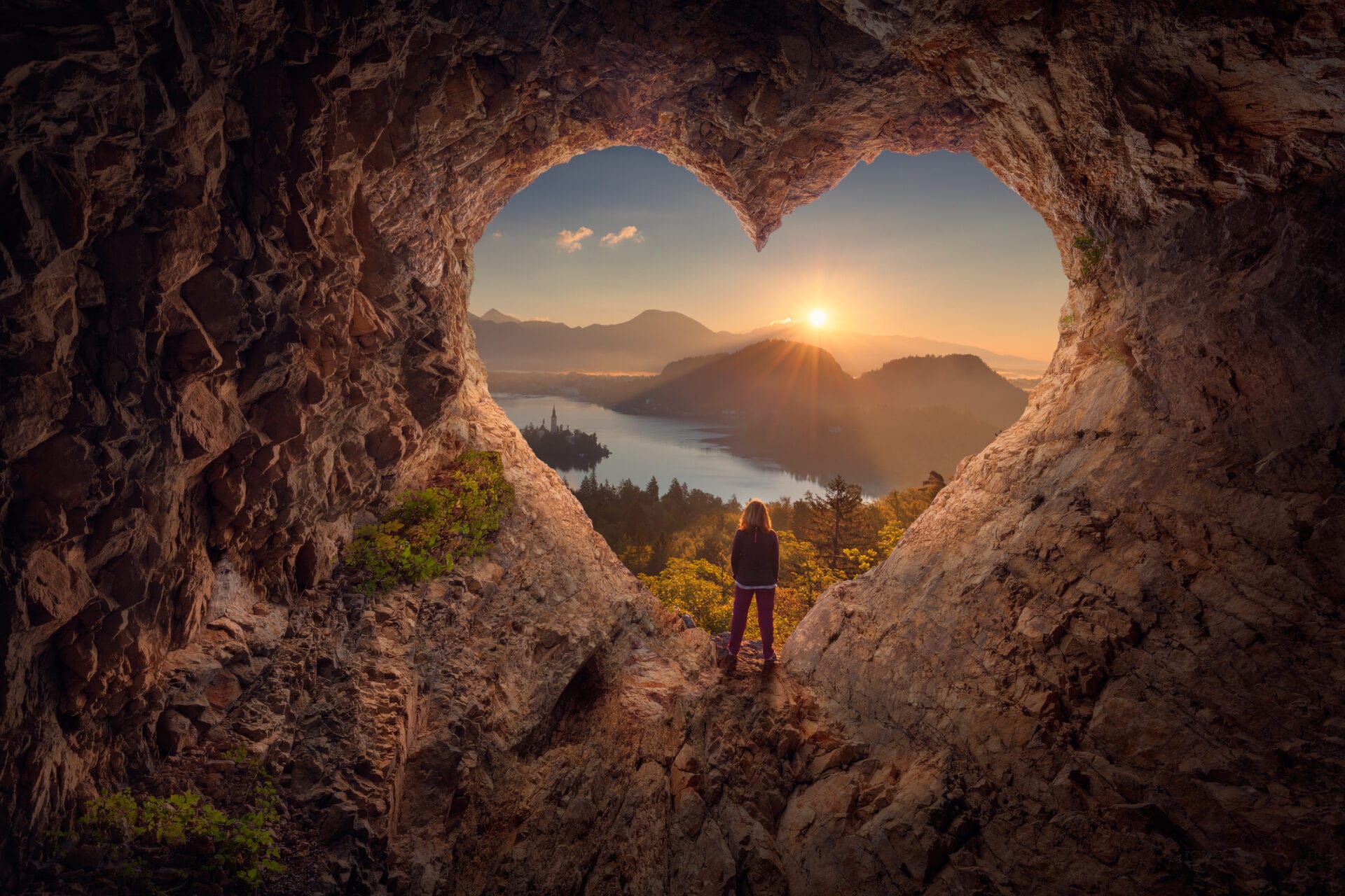 Young woman in heart shape cave towards the idyllic sunrise